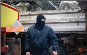  ?? (AP/Visar Kryeziu) ?? A masked Serb watches Thursday as workers remove trucks from a barricade near the northern, Serb-dominated part of ethnically divided town of Mitrovica, Kosovo.