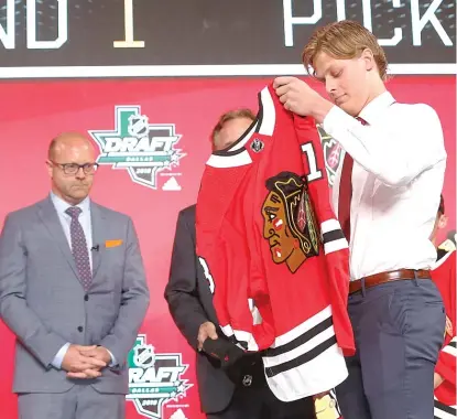  ?? AP ?? GM Stan Bowman watches defenseman Adam Boqvist put on his Hawks sweater after drafting him with the No. 8 pick Friday.