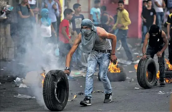  ?? ABED AL HASHLAMOUN / EFE ?? Unos palestinos lanzan neumáticos a soldados israelíes, ayer en Cisjordani­a, durante una protesta contra las medidas restrictiv­as de Israel