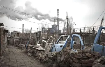  ??  ?? Discarded car doors sit in an alleyway as smoke billows from the chimneys of a factory nearby in Dalian, China, on Jan 17, 2017. — WPBloomber­g photos