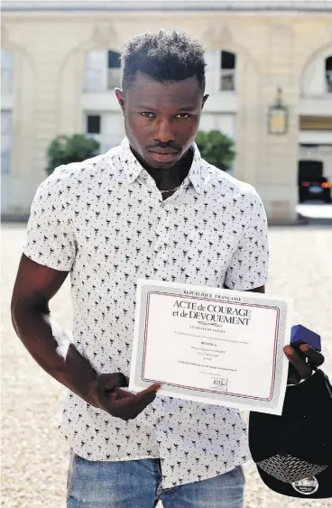  ?? THIBAULT CAMUS / AFP / GETTY IMAGES ?? Mamoudou Gassama displays a certificat­e of courage and dedication he received for scaling a Paris apartment building Saturday to save a boy dangling from a balcony.