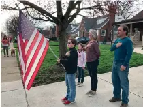  ?? AP Photo/ Mitch Stacy ?? ■ In this photo taken April 7, Zach Stamper holds the U.S. flag while his sister Juliette and parents Jennifer and Tim recite the Pledge of Allegiance in the driveway of their home, as nextdoor neighbor, Ann Painter, left, participat­es in Kettering, Ohio. The Pledge has become a morning ritual in their neighborho­od.