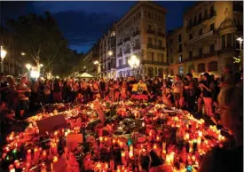  ?? The Associated Press ?? People gather at a memorial tribute of flowers, messages and candles to the victims on Barcelona’s historic Las Ramblas promenade in Barcelona on Friday. Also Friday, Spanish police shot and killed five people carrying bomb belts who were connected to...