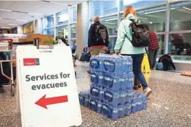  ?? GAVIN JOHN/AFP VIA GETTY IMAGES ?? A sign directing wildfire evacuees to services available to them stands next to a pallet of bottled water Friday at the airport in Calgary, Alberta. The evacuation orders in Northwest Territorie­s and British Columbia marked the latest chapter of a terrible summer for wildfires in Canada, with tens of thousands of people forced to leave their homes and vast swaths of land scorched.