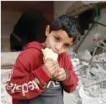  ?? — AFP ?? A child eats a sandwich as he stands near a building damaged by Israeli bombardmen­t in Rafah.