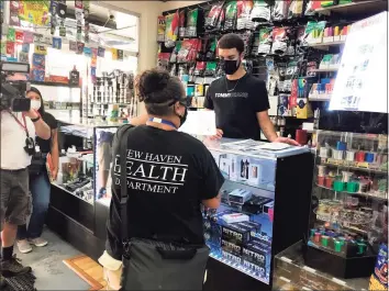  ?? Brian Zahn / Hearst Connecticu­t Media ?? New Haven Senior Sanitarian Shellie Longo provides signs for Grab ‘N Go Mart Smoke Stop clerk Zael Cortes to display around the store on Tuesday during a canvass of downtown businesses.