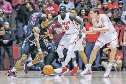  ?? PHOTOS BY JUAN ANTONIO LABRECHE/THE ASSOCIATED PRESS ?? New Mexico State’s AJ Harris, front left, drives around Johnathon Wilkins, behind left, and is met by New Mexico’s Makuach Maluach, center, and Joe Furstinger, right, during Saturday’s game in The Pit. NMSU won 65-62.