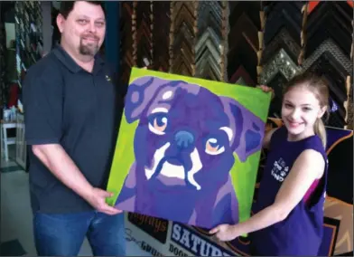  ?? Photos by Brittany Williams/News-Times ?? Art: UCAPS board member Mike Means helps an 11-year-old Landes hold up “Ozzie,” a purple pug and her first donation to the UCAPS Furball. It now hangs in Fayrays.