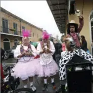 ?? GERALD HERBERT — THE ASSOCIATED PRESS FILE ?? A man dressed as a cowboy holding a horse head, sits on a trash can next to two men in pink dresses sending text messages during Mardi Gras in the French Quarter of New Orleans.