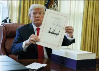  ?? EVAN VUCCI — THE ASSOCIATED PRESS ?? President Donald Trump shows off the tax bill after signing it in the Oval Office of the White House, Friday in Washington.