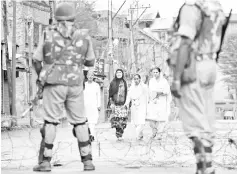  ?? — AFP photo ?? Indian paramilita­ry troopers standing guard as Kashmiri pedestrian­s walk along a road during restrictio­ns after Kashmiri separatist­s called for a one-day strike to protest a civilian killing in Srinagar in this file photo.