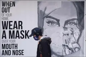  ?? Jeff Chiu / Associated Press ?? A pedestrian walks past a mural reading, “When out of your home, Wear a mask over your mouth and nose,” in San Francisco in November.