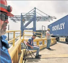  ??  ?? STUCK: Workers watch as containers full of emergency supplies are unloaded from a barge and onto a port in San Juan.