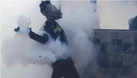  ?? — AP ?? CARACAS: A masked anti-government protester lobs a tear gas canister launched by security forces during clashes in Caracas, Venezuela.