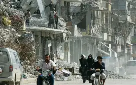  ?? (Aboud Hamam/Reuters) ?? PEOPLE RIDE BY damaged buildings last month in Raqqa, Syria.