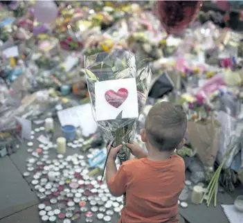  ?? EMILIO MORENATTI/THE ASSOCIATED PRESS ?? A child places flowers in a square in central Manchester, Britain, on Wednesday.