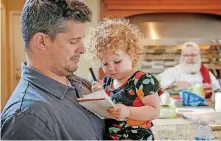  ??  ?? Army Chief Warrant Officer Ryan Davis holds his daughter, Madelyn, as Larry Zillox works in the kitchen to help prepare dinner near Haymarket, Virginia.