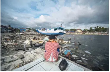  ?? — AFP ?? Deep in thought: A resident looking at a washed up boat amid a scene of destructio­n at Wani, Sulawesi.