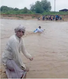  ?? — AFP ?? People trying to cross flood waters in Deesa municipali­ty, which has been hit by severe flooding along the Banas River in Gujarat.