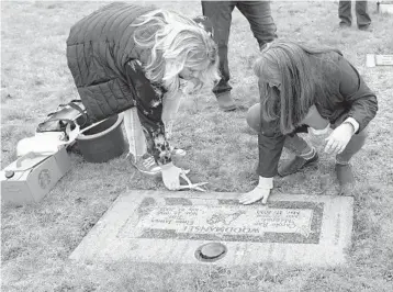 ?? TED S. WARREN/AP ?? Wendy Jensen, left, and Bonnie Dawson trim grass and clean the headstone of their mother, Carole Rae Woodmansee, on March 27 to mark one year since her death from COVID-19. Woodmansee died on her 81st birthday.