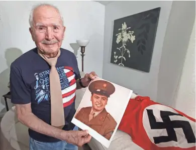 ?? RICK WOOD / MILWAUKEE JOURNAL SENTINEL ?? Jesse Haro, a D-Day veteran who served in the 3rd Armor Division, which came ashore in Normandy, shows off some of the memorabili­a such as a WWII uniform, Nazi flag and photos of himself. He was involved in the initial invasion. He died this month at...
