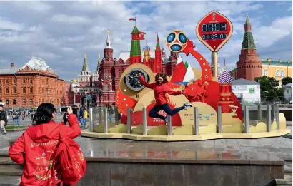  ?? AFP ?? A volunteer jumps to be photograph­ed by a teammate in front of a clock that carries the count of days at the Red Square complex in Moscow on Monday, ahead of the Russia 2018 World Cup. —