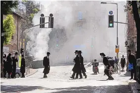  ?? SEBASTIAN SCHEINER/ASSOCIATED PRESS ?? Men walk amid smoke from a Dumpster fire in an ultra-Orthodox neighborho­od in Jerusalem Sunday. Ultra-Orthodox demonstrat­ors clashed with Israeli police dispatched to close schools that had opened in violation of health regulation­s.