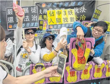  ?? AFP ?? Pro-government protesters use slippers to beat pictures of the leaders of the Umbrella Movement outside the Eastern District Court in Hong Kong yesterday.