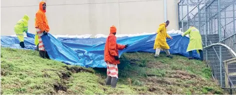  ??  ?? Jail trusties and deputies put out a tarp over the landslide, before putting out sandbags to help support the soggy ground between the Circuit Court building and the county jail on Tuesday. (Photo by Ryan Phillips, SDN)