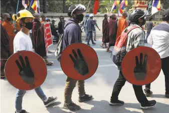  ?? Associated Press ?? Demonstrat­ors carry shields painted with the threefinge­r sign of resistance during a coup protest in Mandalay. The world community is under pressure to restrain the military junta.