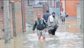  ?? WASEEM ANDRABI/HT ?? Men wade through a flooded street in Srinagar on Friday. Rain and snow in the Valley for three days have led to swollen rivers and streams. The water level in Jhelum river has started to recede but is still flowing above the danger mark at Ram Munshi...