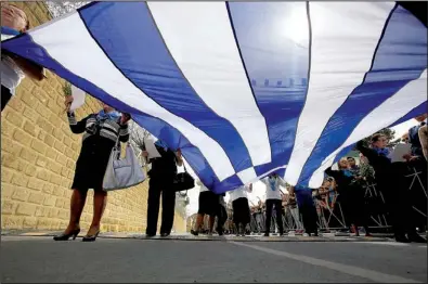  ?? AP/PETROS KARADJIAS ?? Women hold a Greek flag Monday during a wreath-laying ceremony at a memorial in Nicosia for those killed in the country’s fight against British colonial rule in the late 1950s. Cyprus now has until 2017 to reach a targeted budget surplus of 4 percent...