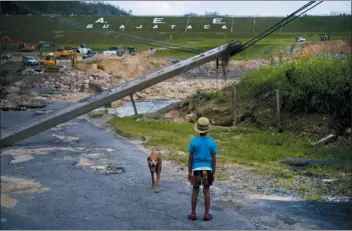  ?? RAMON ESPINOSA — THE ASSOCIATED PRESS ?? In this file photo, a boy accompanie­d by his dog watches the repairs of Guajataca Dam, which cracked during the passage of Hurricane Maria, in Quebradill­as, Puerto Rico. Experts said on Thursday that Puerto Rico could face nearly two decades of further economic stagnation and a steep drop in population as a result of Maria.