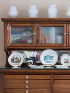  ??  ?? Right: Pat converted a former dental cabinet with glass knobs into a dining room hutch. The arrangemen­t of ironstone vases on top parallels that of the souvenir plates and vessels below. The shallow drawers, which Pat lined with tarnish-preventing fabric, hold silverware and napkin rings.
