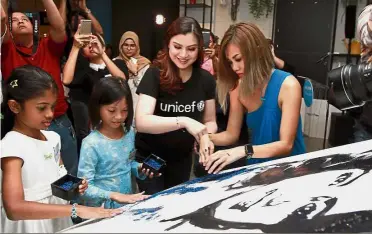  ??  ?? Global role: Lisa putting the finishing touch on artist Haze Leong’s painting to officiate her appointmen­t. Helping them are (from left) Serene Zara Taufiq and Medina Zaharah.