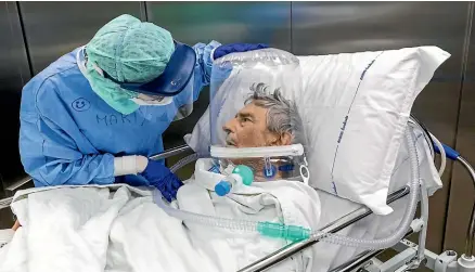  ?? MARCO DI LAURO/GETTY IMAGES ?? A nurse in an Italian hospital attends to a Covid-19 patient wearing an oxygen helmet while he is moved out of intensive care.