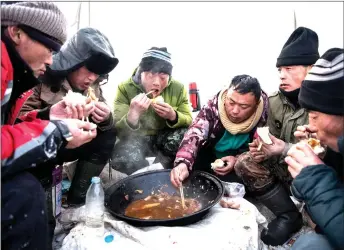  ??  ?? Liu (centre) and his colleagues eating during a lunch break from cutting ice blocks.