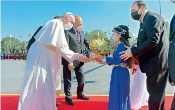  ?? AFP ?? An Iraqi girl in a traditiona­l dress offers Pope Francis a bouquet of flowers at Baghdad airport upon his arrival on Friday. Pope Francis is honouring the victims of one of Iraq's most brutal massacres of Christians by Islamic militants by saying their deaths are a reminder that violence is incompatib­le with religious teaching. —