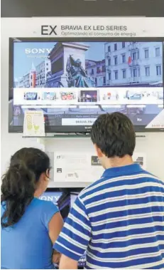  ??  ?? ► Dos personas frente a un televisor en una tienda en Santiago.