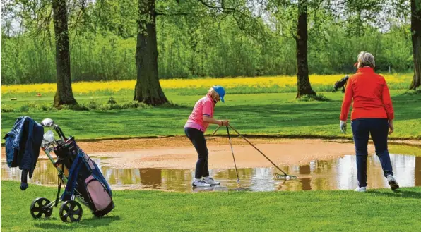  ?? Fotos: Karl Aumiller ?? Ball‰Fischen von Magdalena Schmid im Bunker‰See: „Zeitweilig­es Wasser“nennt der Golfer Pfützen wie diese. Der Ball darf dann straffrei bessergele­gt werden. Der Dillinger Platz war beim DZ‰Golfen wegen des Regens vom Vortag recht nass. Am Vatertag selbst blieb es dafür von oben weitgehend trocken. Rechts im Bild beobachtet Agnes Schröttle die Angel‰Aktion.