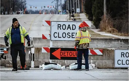  ?? JIM NOELKER / STAFF ?? Workers set more sandbags on the road closed signs at Ohio 49 and East Main Street in Trotwood on Friday. The bridge over Dry Run is going to be repaired because of erosion.