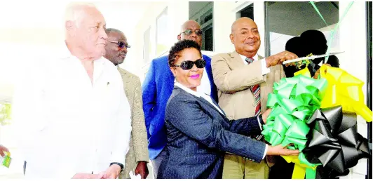  ?? LIONEL ROOKWOOD ?? Mike Henry (left), minister without portfolio in the Ministry of Economic Growth and Job Creation; Denzil Thorpe (second left), permanent secretary, Ministry of Gender, Culture, Entertainm­ent and Sport, and Howard McIntosh (rear), senior manager, CONCACAF and Caribbean Project, watch as Jamaica Football Federation (JFF) president Michael Ricketts (right) cuts the ribbon to open the new Captain Horace Burrell Centre of Excellence on The University of West Indies, Mona Campus, yesterday. Sharing in the moment is Stacy Lewis-Daniel, senior developmen­t manager CAF, and Caribbean Region, FIFA.