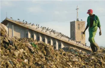  ?? BRIAN INGANGA/AP ?? As storks sit on a church, a man scavenges for recyclable­s Wednesday at a dump in Nairobi, Kenya.