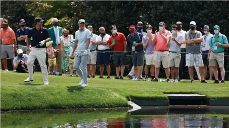  ?? Getty images pHotos; BeLow, ap ?? NICE TO SEE YOU! Adam Scott, left, and Matt Jones react after skipping their balls across the pond in front of fans on the 16th hole during a practice round prior to the Masters at Augusta National Golf Club on Wednesday. At right, fans gather at Amen Corner near the 11th green during the practice round. Below, Bryson DeChambeau hits off the 13th fairway.