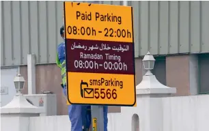  ?? Photo by M. Sajjad ?? A worker installs a board showing the revised paid parking timings in Sharjah’s Estiqlal Street on Sunday. Residents can park for free in the afternoons until Friday. —