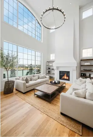  ??  ?? A full-height, 24-foot gas fireplace chase enhances the great room where viewscale mullioned windows overlook the lake and beach club beyond. Clerestory windows and a period-style chandelier lend additional light.