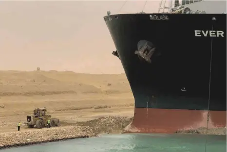  ?? FOTO: SUEZ CANAL AUTHORITY VIA EGYPTIAN CABINET FACEBOOK PAGE/DPA ?? Mühsame Arbeit: Ein Bagger versucht, den Bug des Containers­chiffs Ever Given zu befreien, nachdem es im südlichen Ende des Suezkanals auf Grund gelaufen ist und den Schiffsver­kehr in beide Richtungen blockiert.