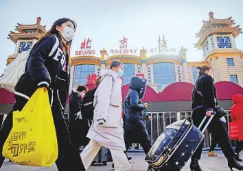  ?? AP ?? Travellers wearing face masks walk past the entrance of the Beijing Railway Station yesterday. Millions of Chinese are expected to travel during the Lunar New Year holiday period this year.