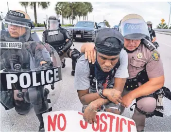  ?? FOTO: DPA ?? Ein Mitarbeite­r der Florida Highway Patrol und Polizisten knien in Boca Raton mit einem Demonstran­ten nieder.