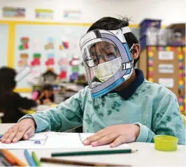  ?? MARCIO JOSE SANCHEZ / AP ?? A student wears a mask and face shield in a fourth-grade class amid the COVID-19 pandemic in 2022 at Washington Elementary School in Lynwood, California. Four years after the COVID-19 pandemic closed schools across the country and upended child care, the CDC says parents can start treating the virus the way they do other respirator­y illnesses.